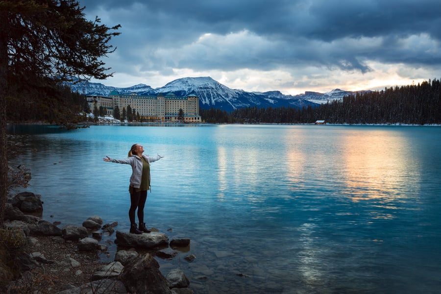 person with arms held open stands on the edge of a body of water