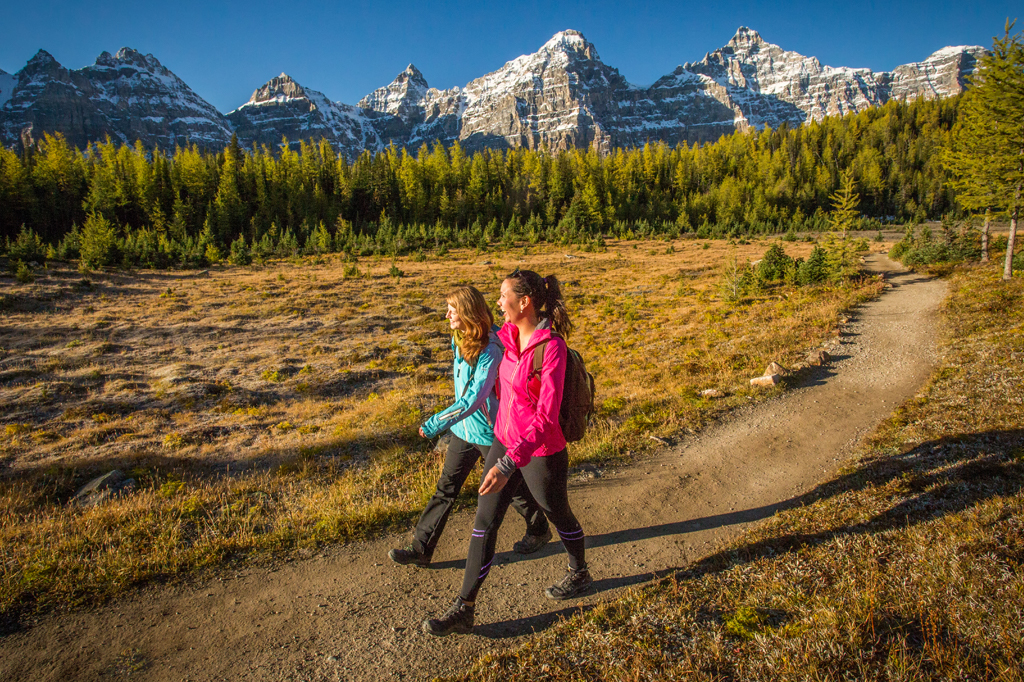 two people hiking in a grassy area with mountains in the background