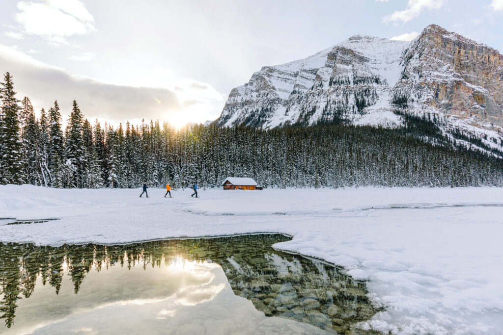 people walk outside in winter in front of chalet with mountains in the background