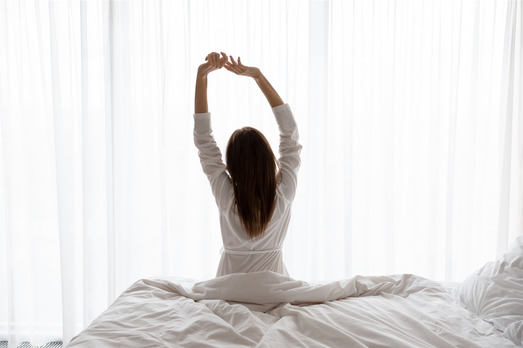 Beautiful woman sitting on bed, stretching arms in the morning