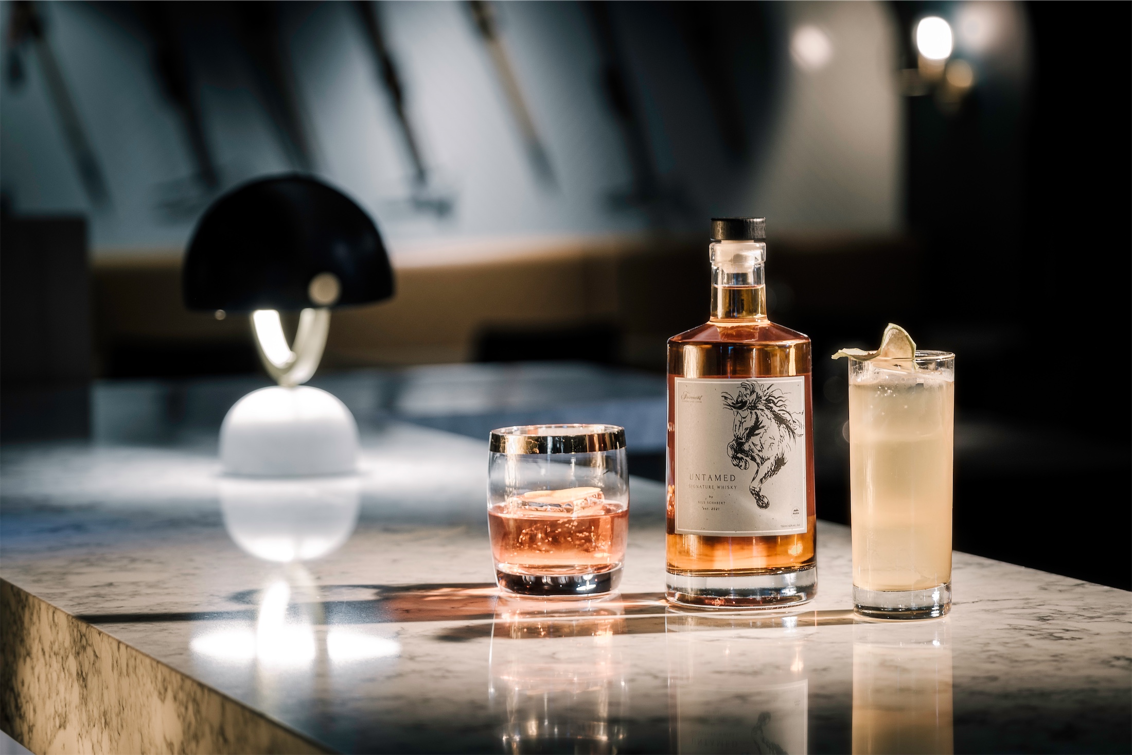 a bottle of whiskey in between two whiskey cocktails
