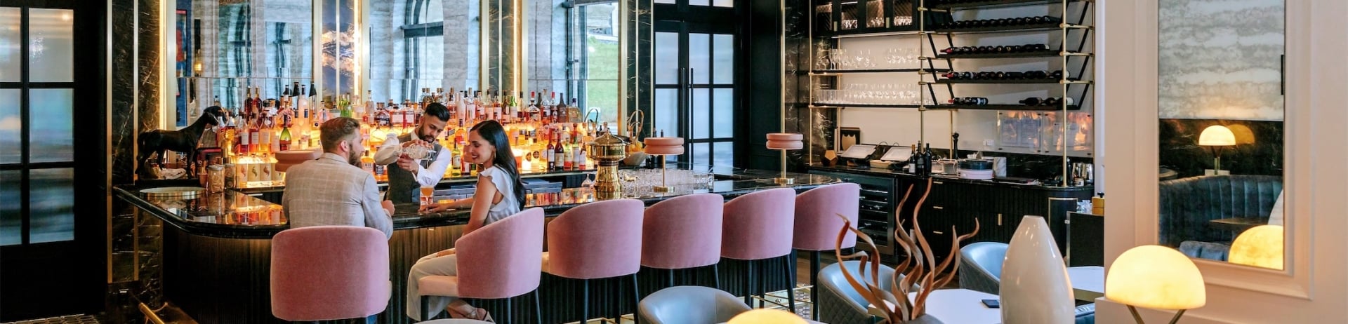 a couple sitting in pink chairs while the bartender mixes drinks