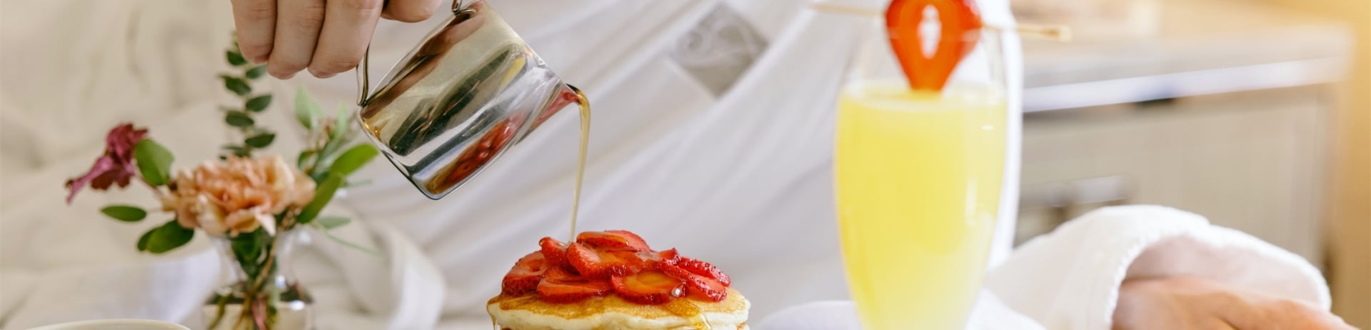 man pouring syrup over a stack of pancakes