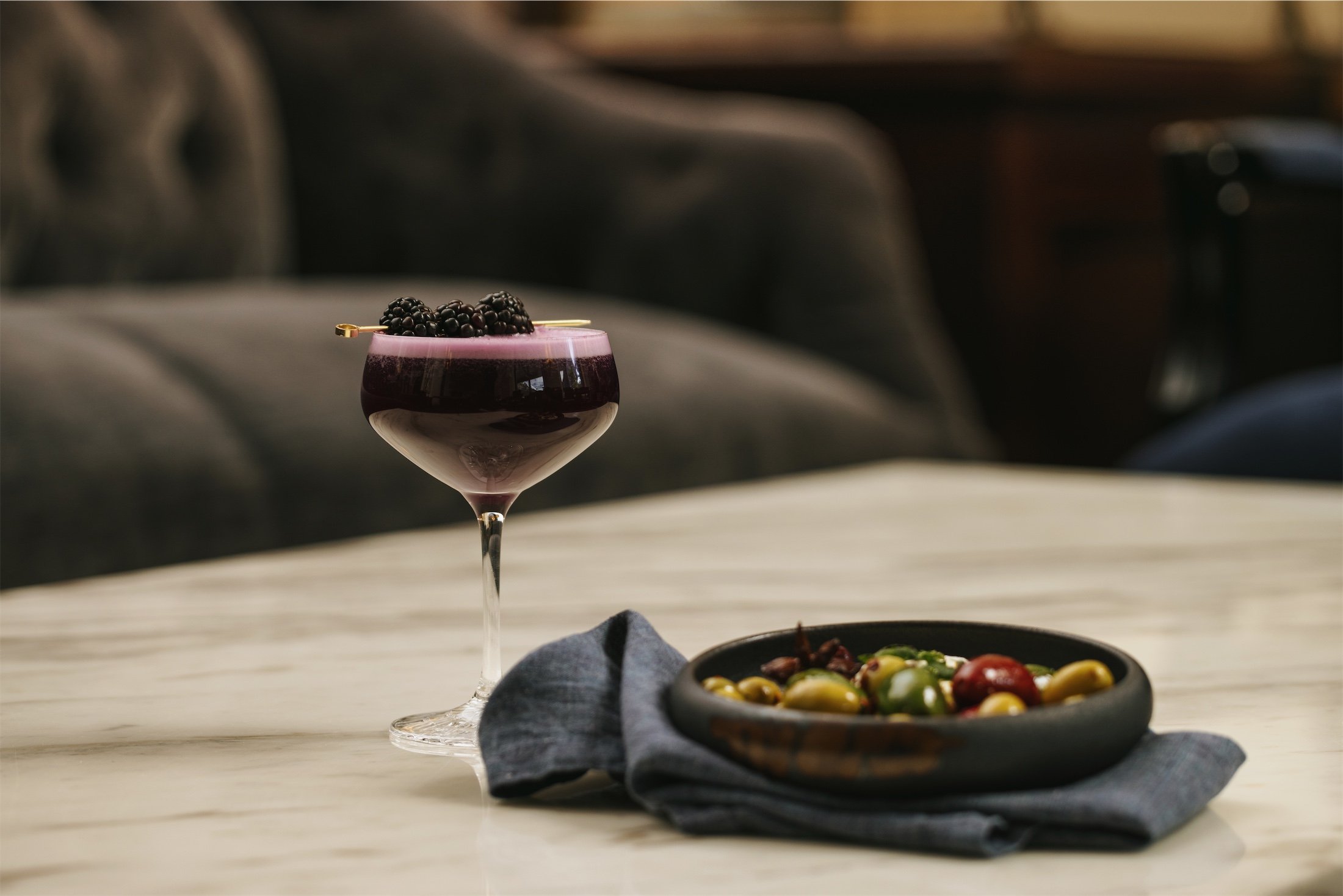 olive dish next to a purple cocktail