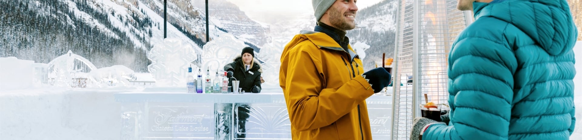 couple standing by the outdoor heater drinking hot drinks at the ice bar