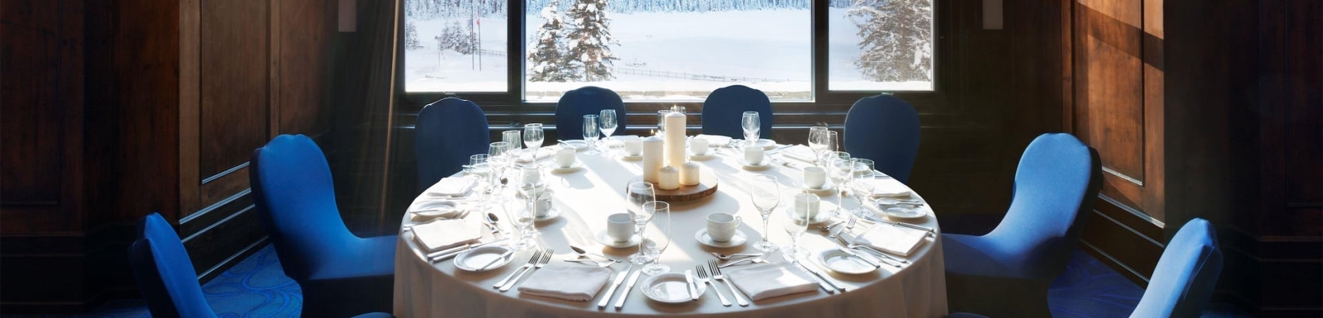 A round table set with dinnerware in front of a large window with mountain views
