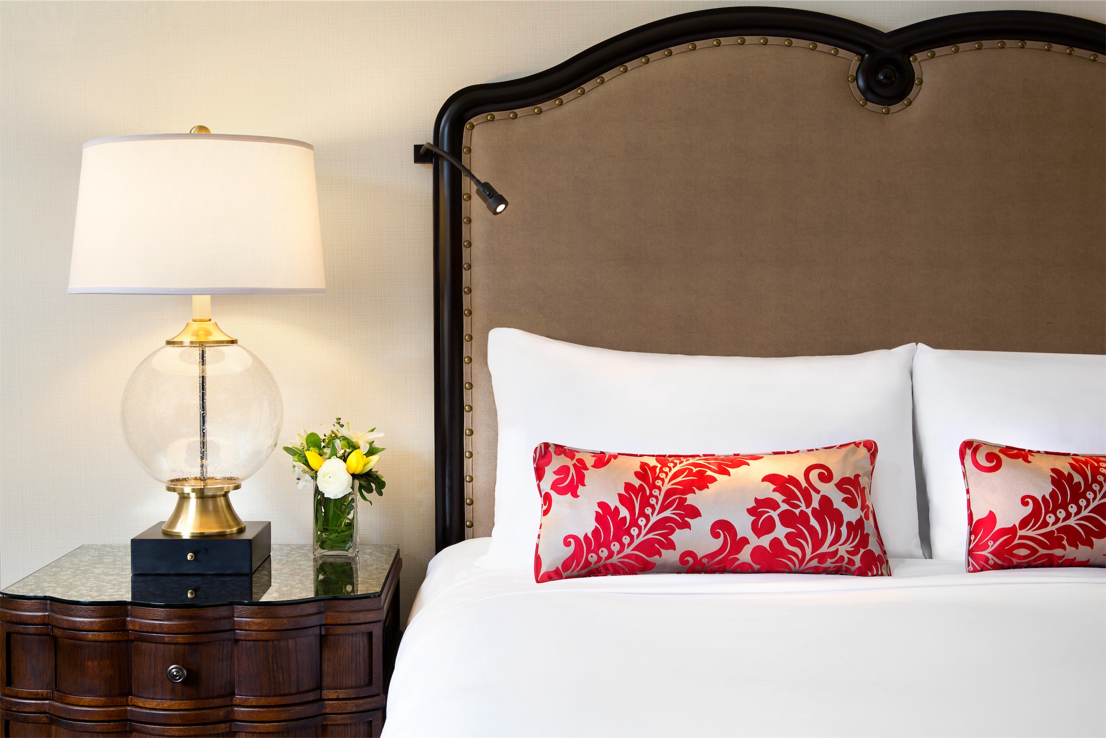 close up of pillows on a bed and flowers on a nightstand