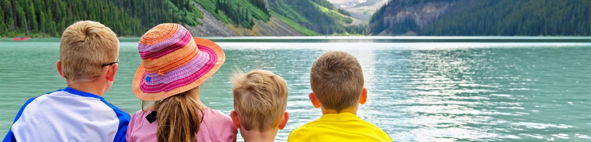 four children sitting on a rock looking out at the lake