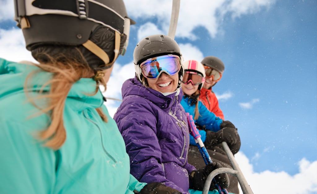 four people in multi-coloured jackets wearing goggles and helmets sit in a chair lift