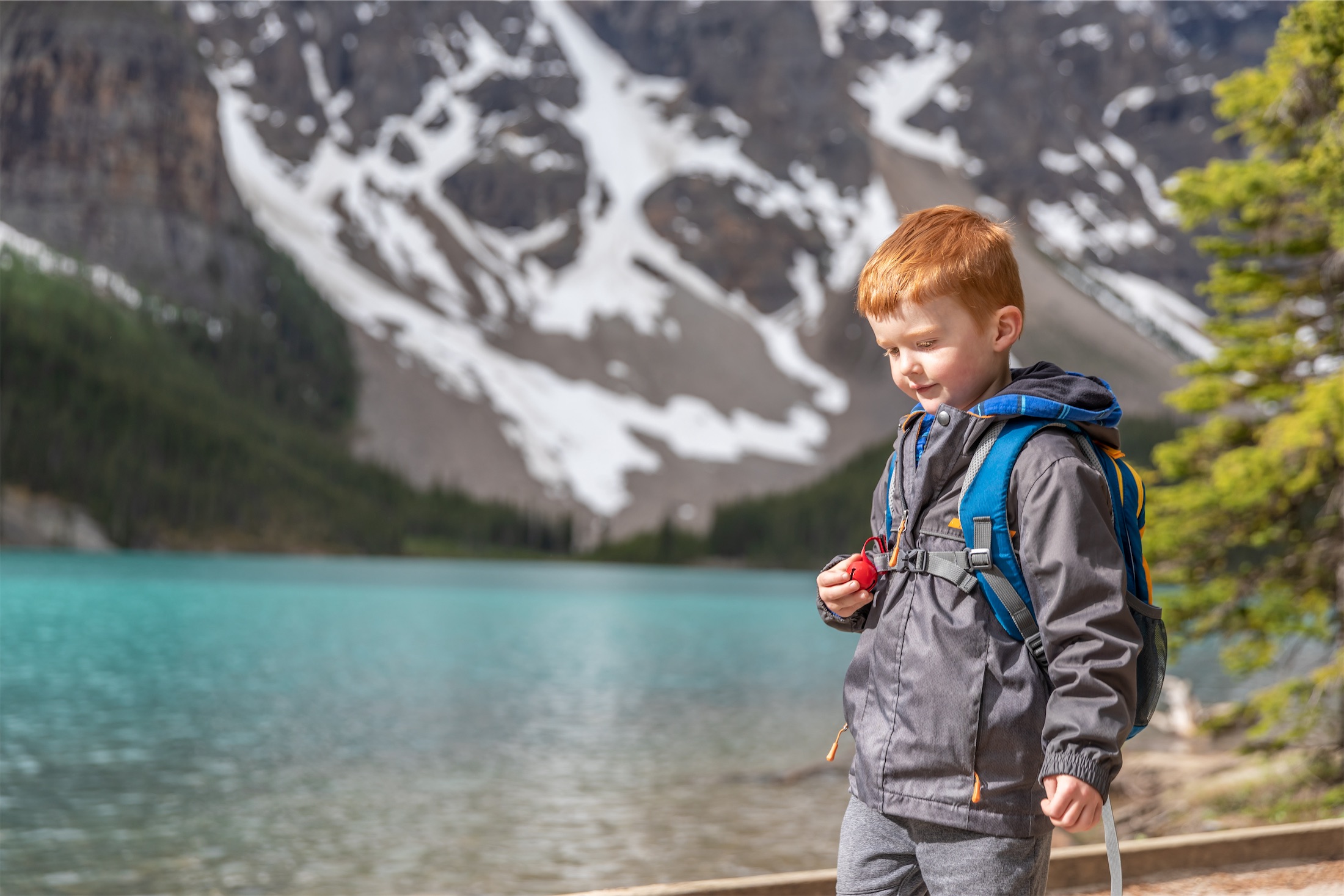 kid walks alongside water with snow covered mountain in background