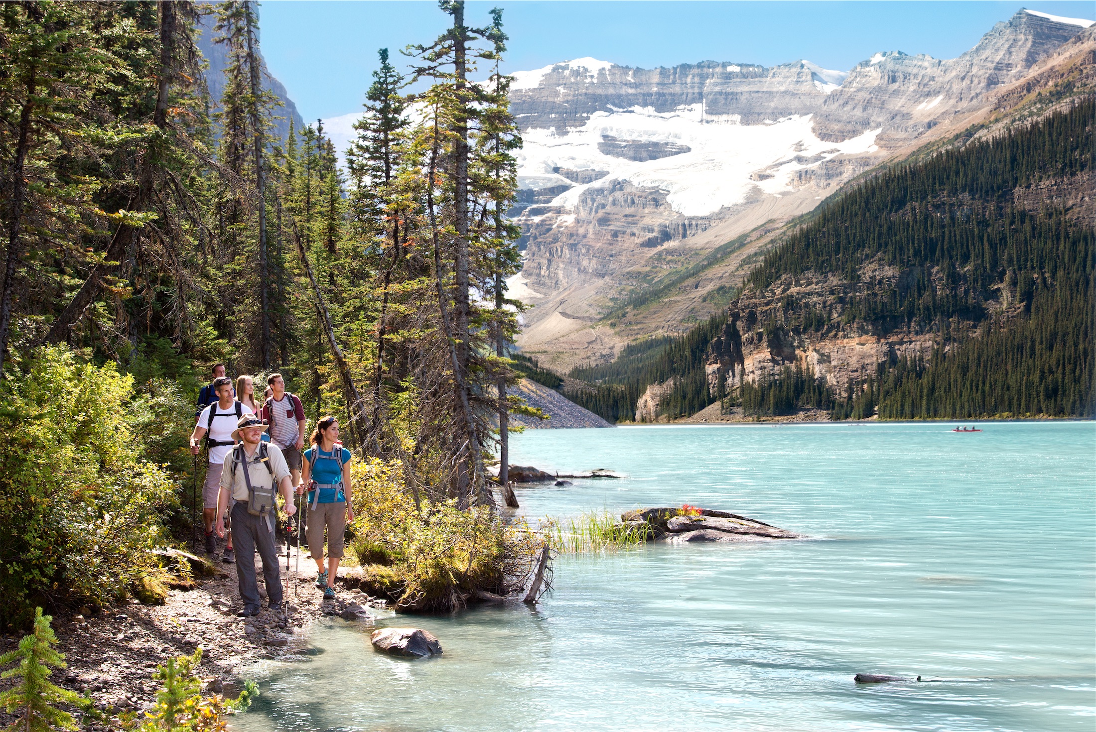 person walks along water with trees and mountain in the background