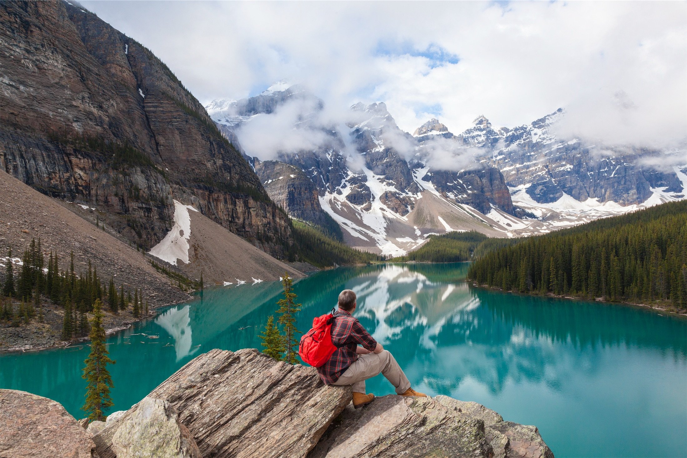 person hiking sits on a rocky edge with lake and mountains in the background