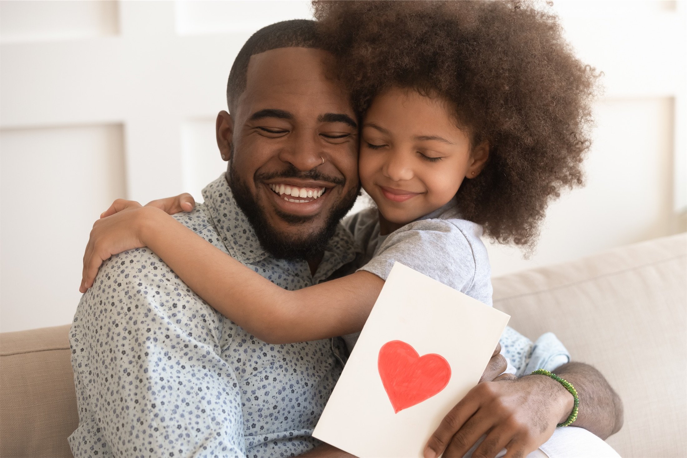 girl hugs father while holding a card with heart on it