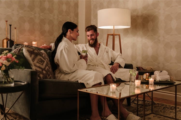 A couple in robes on a loveseat surrounded by candles