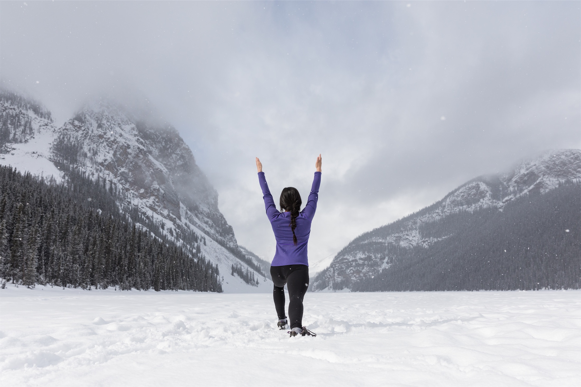 A woman doing yoga in the snow surrounded by mountains