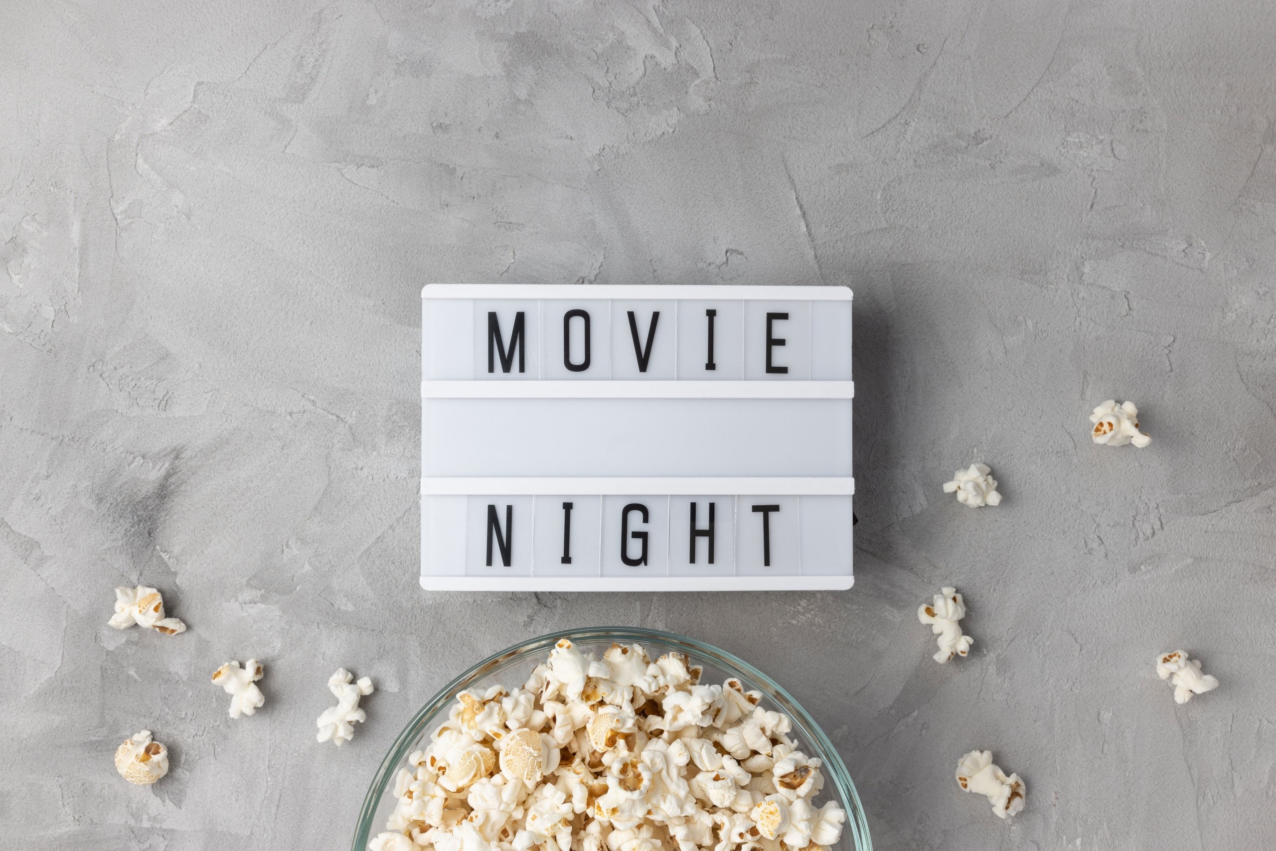 bowl of popcorn with loose kernels spread around and a movie night sign