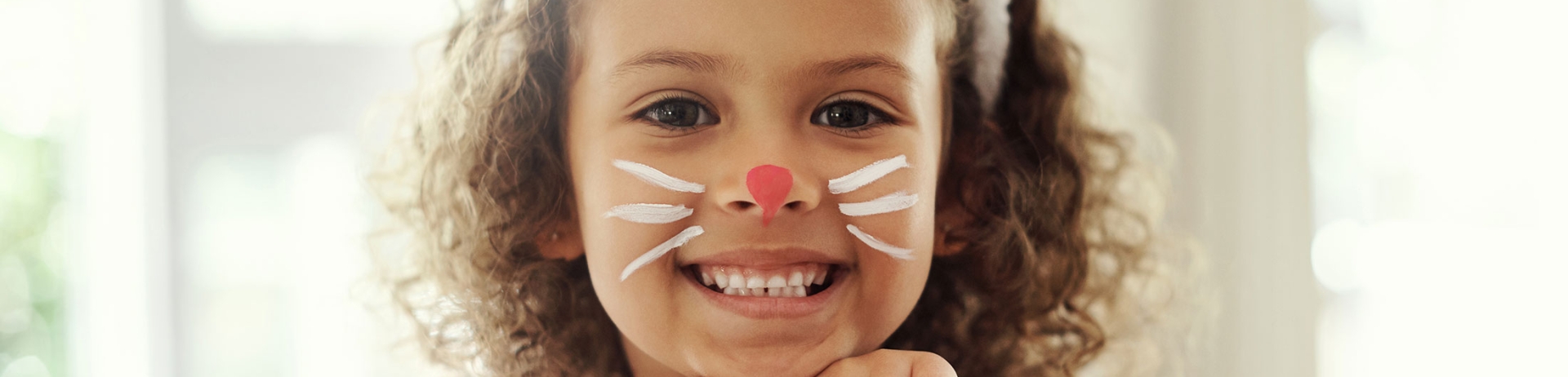 Child with face painted with whisker and a red nose and a bunny ears headband