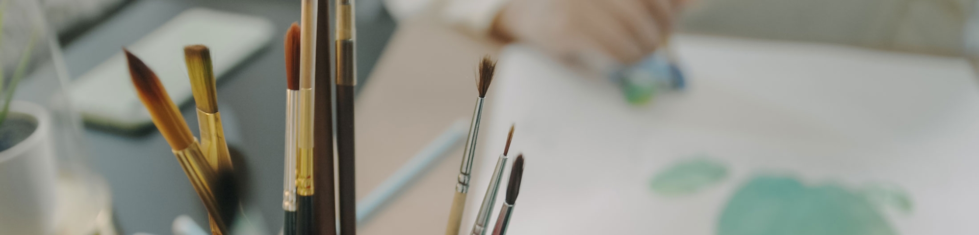 Bucket of paintbrushes with a water colour image out of focus in the background