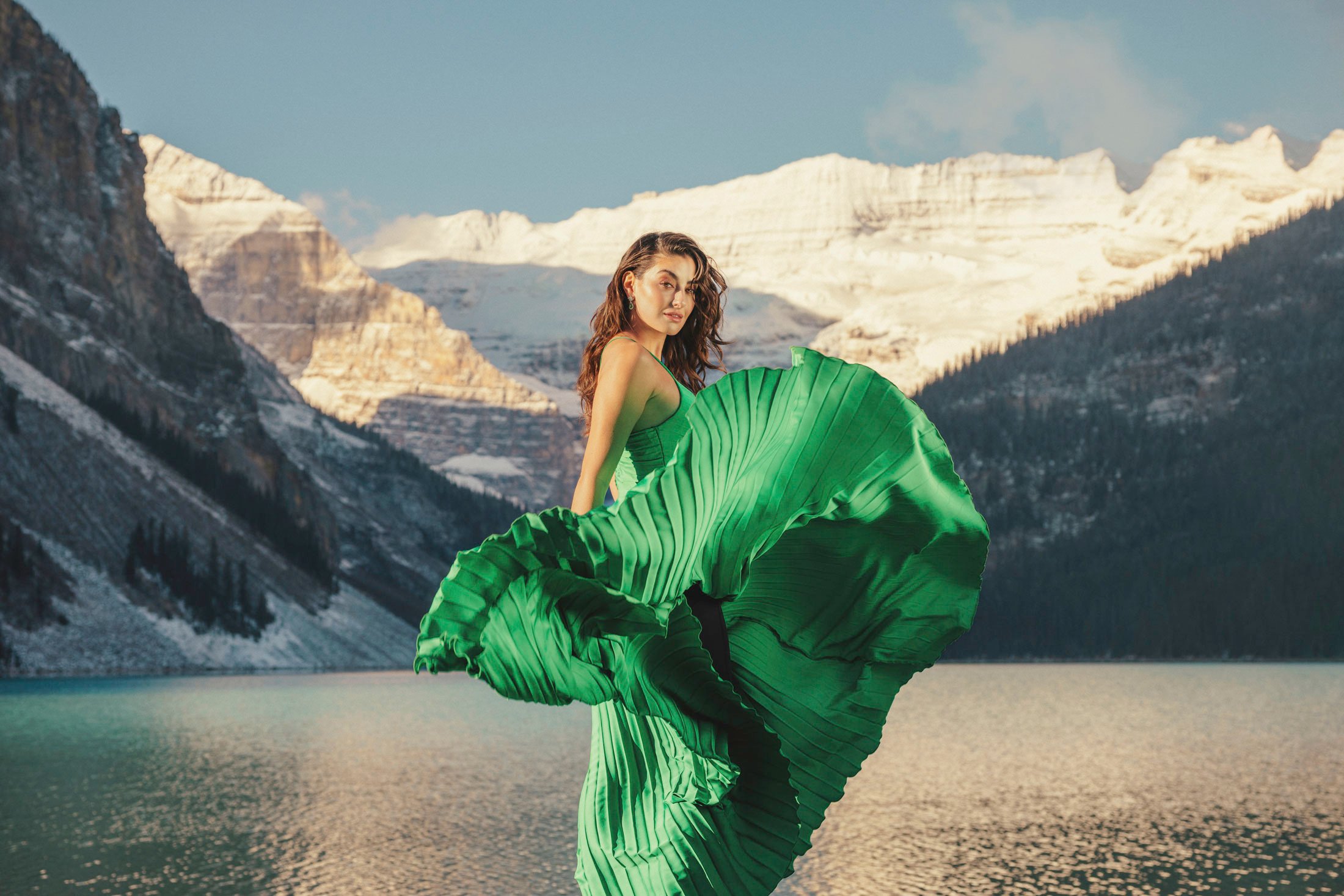 Woman twirls her green dress in front of Lake Louise as the sun rises