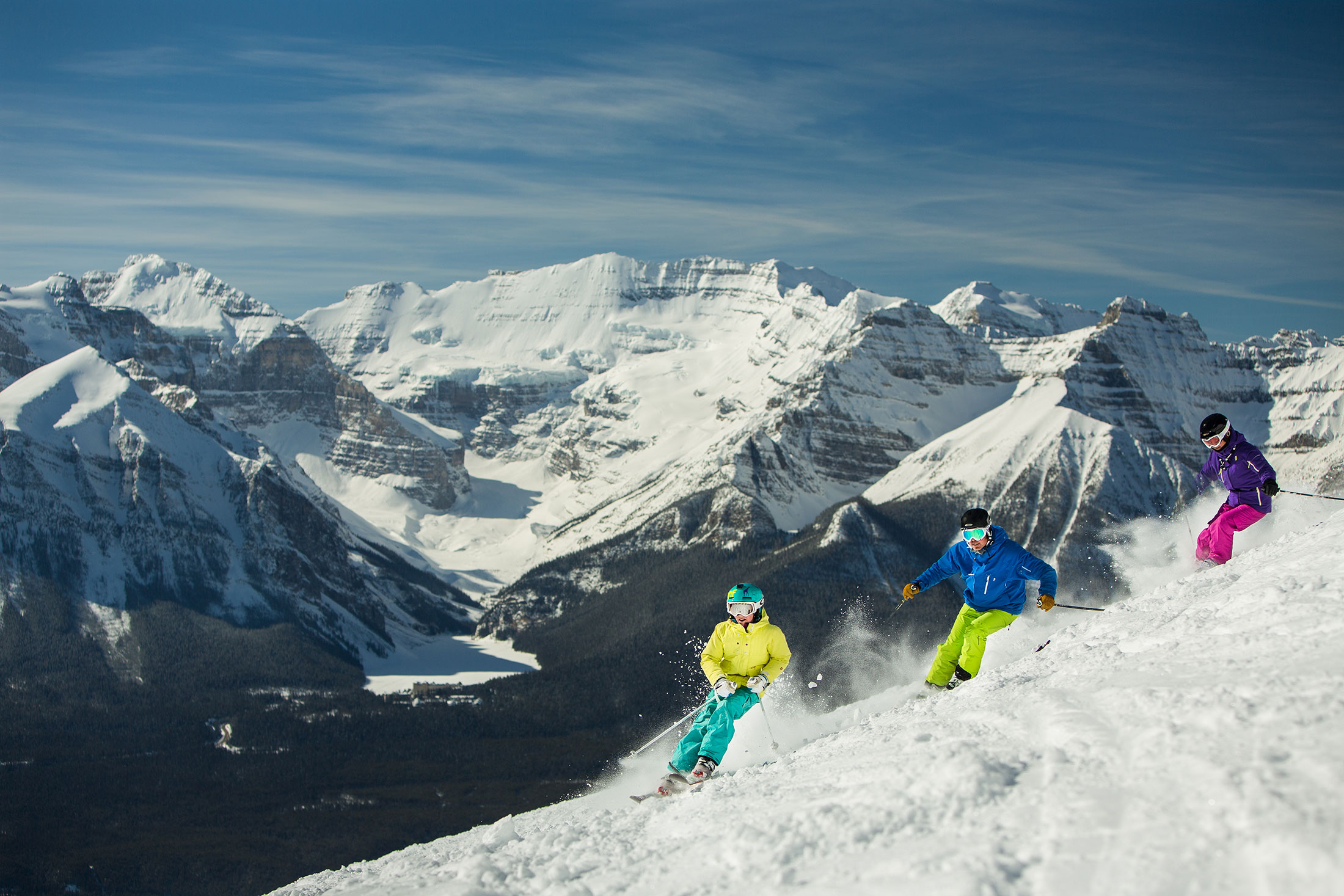 Three Skiers on Lake Louise Ski Resort with blue clear mountains in the background.