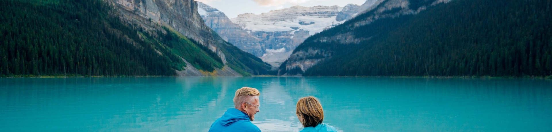 A couple sitting along the lakeshore looking out at Lake Louise.