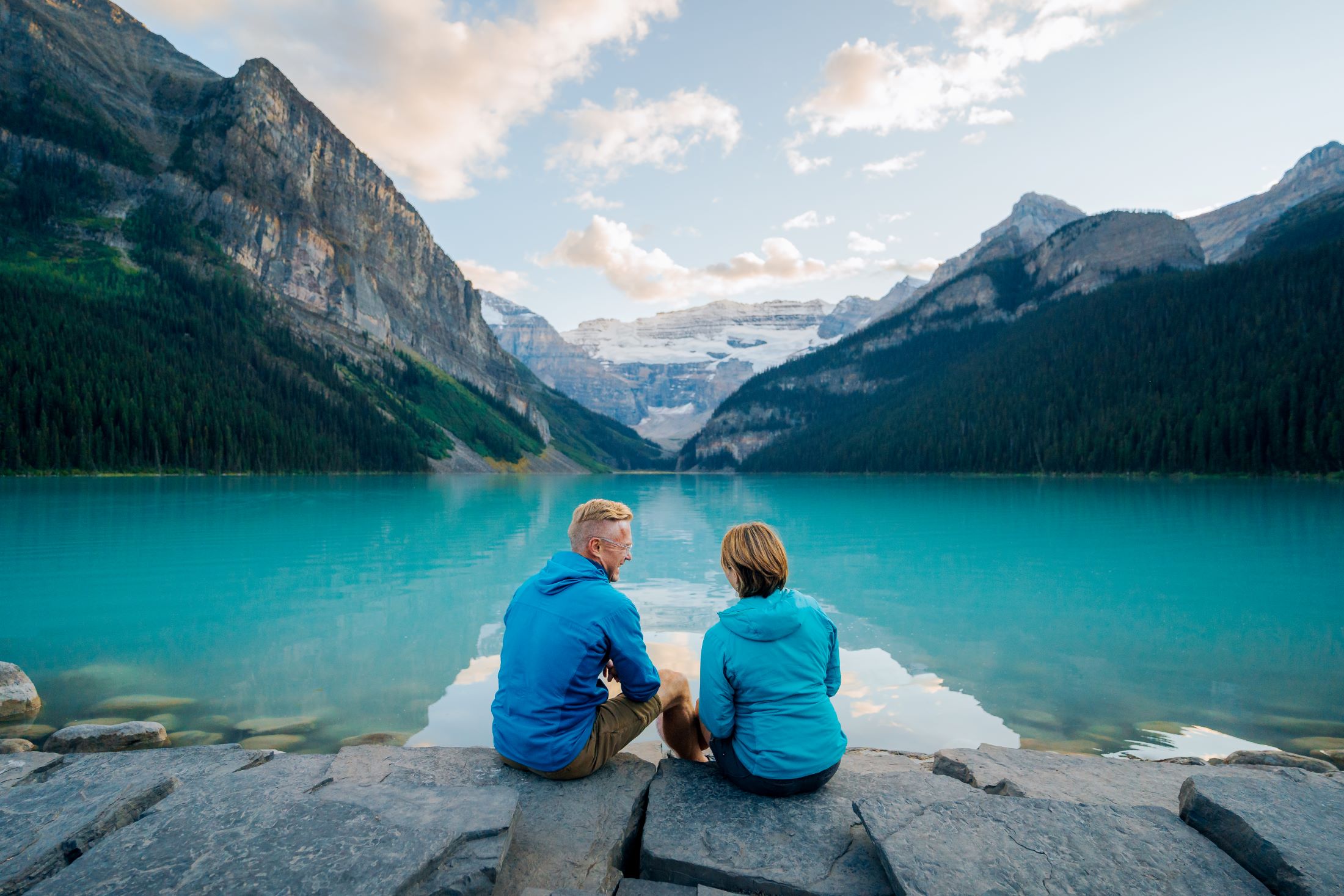A couple sitting along the lakeshore looking out at Lake Louise.