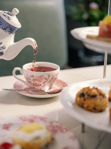 Pouring tea into teacup with scones in background